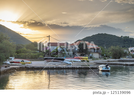 Mali Ston, village in Peljesac peninsula in Croatia, Europe. Tranquil waterfront scene with beached boats and houses bathed in soft sunlight, backed by mountains and a serene sky. 125139096