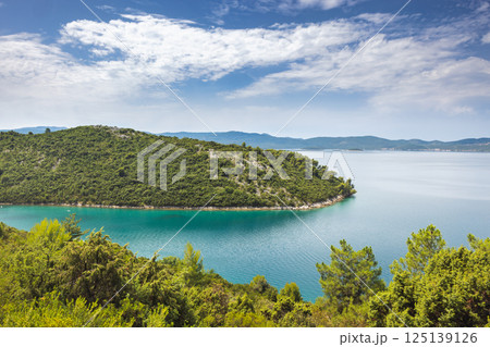 The sea coast of southern Dalmatia in Croatia, Europe. Scenic coastal view: Lush green island meets turquoise waters under a partly cloudy sky. Perfect for nature lovers and exploration. 125139126