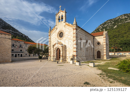 Ston, historic town in Peljesac peninsula in Croatia, Europe. Picturesque church nestled in serene landscape under clear sky, architectural elegance meets tranquil nature backdrop. Timeless beauty! 125139127