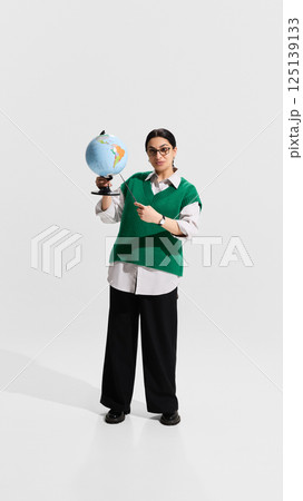 Teacher holding globe and pointer while explaining geography lesson with confident posture. Teacher holding globe and pointer while explaining geography lesson with confident posture. 125139133
