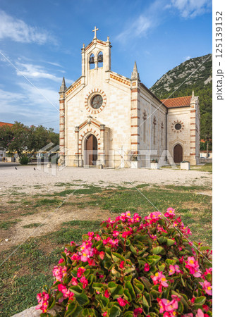 Ston, historic town in Peljesac peninsula in Croatia, Europe. Historic church with a bell tower stands tall against a blue sky, framed by pink flowers. Tranquil scene of architecture. 125139152