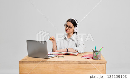 Focused female teacher in white shirt and headphones explaining subject during online lesson with expressive gesture. 125139198