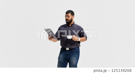 Calm male educator holding coffee cup and tablet, reading attentively, symbolizing thoughtful analysis, digital literacy and relaxed professionalism Calm male educator holding coffee cup and tablet, reading attentively, symbolizing thoughtful analysis, digital literacy and relaxed professionalism 125139208