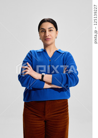 Portrait of focused woman, teacher in blue knitwear crossing arms and standing firmly, conveying leadership, certainty and academic discipline 125139227