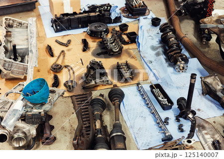 Disassembled engine components spread across workshop floor showing crankshaft, driveshaft, chains, housing and tools. Vehicle check-up and repair. Underbody chassis and suspension parts Disassembled engine components spread across workshop floor showing crankshaft, driveshaft, chains, housing and tools. Vehicle check-up and repair. Underbody chassis and suspension parts 125140007