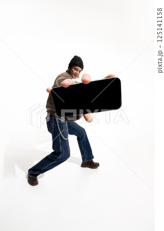 Man in casual streetwear and beanie holds smartphone mockup against white studio background. 125141158