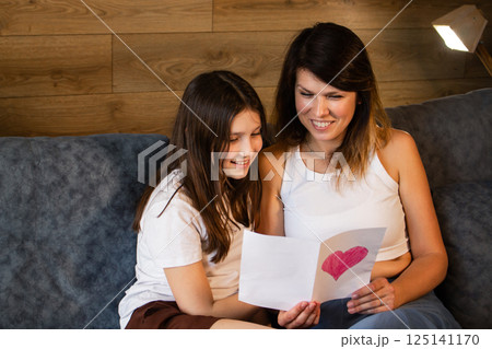 Teenage girl gave mom greeting card for mother's day. Young mother holding handmade gift from daughter. 125141170
