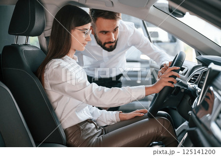 Checking the salon of automobile. Man with woman in white clothes are in the car dealership together 125141200