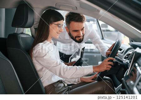 Woman sitting in the automobile. Man in white clothes are in the car dealership Woman sitting in the automobile. Man in white clothes are in the car dealership 125141201