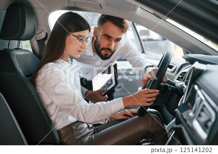 Woman sitting in the automobile. Man in white clothes are in the car dealership 125141202