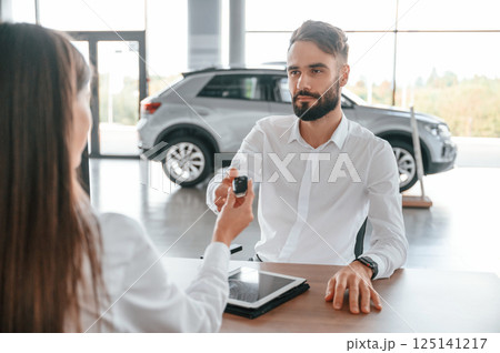 Automobile keys for the new owner. Man with woman in white clothes are in the car dealership together Automobile keys for the new owner. Man with woman in white clothes are in the car dealership together 125141217