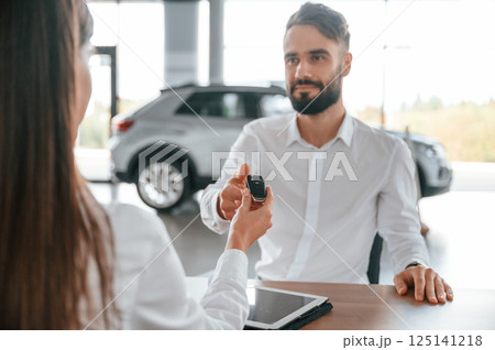 Automobile keys for the new owner. Man with woman in white clothes are in the car dealership together 125141218