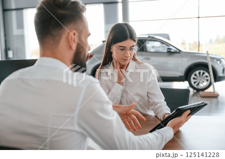 Making a deal. Sitting by the table. Man with woman in white clothes are in the car dealership together 125141228