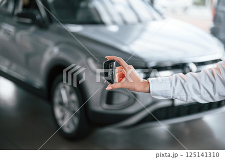 Close up view of keys. Young woman in white formal clothes is in the at dealership Close up view of keys. Young woman in white formal clothes is in the at dealership 125141310
