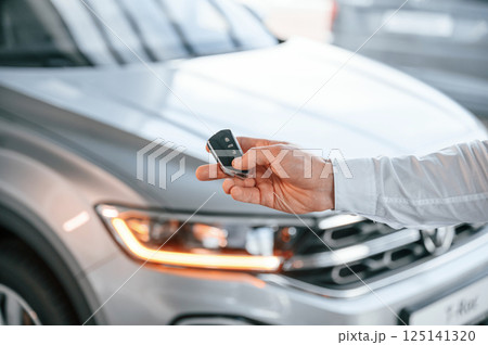 Keys and remote controller. Close up view. Young man in white clothes is in the car dealership 125141320