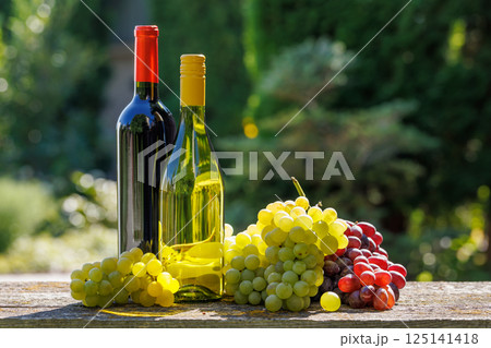 A basket filled with various types of grapes and bottles of red and white wine 125141418