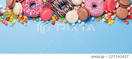 An assortment of colorful sweets, including donuts, macarons, and candies, arranged on a vibrant blue background An assortment of colorful sweets, including donuts, macarons, and candies, arranged on a vibrant blue background 125141437