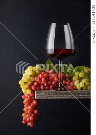 A glass of wine paired with grapes, set against a dark background 125141439
