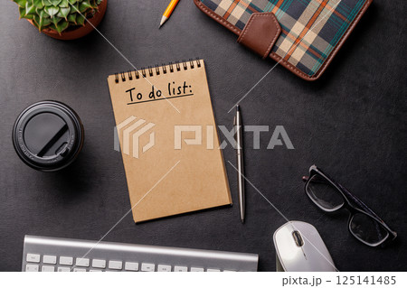Organized work desk setup with PC, office supplies, coffee, and a notepad for writing a to-do list 125141485