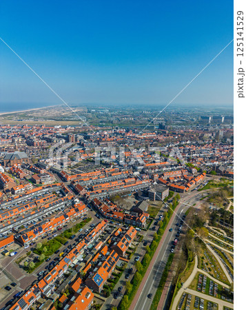 A stunning aerial view of a coastal town with red-tiled rooftops, neatly aligned houses, and a vast sandy beach stretching into the distance under a clear blue sky. 125141529