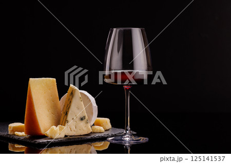 A refined selection of aged cheeses presented on a board, accompanied by a glasses of wine 125141537