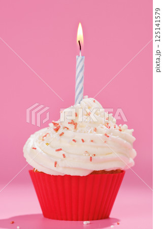 Festive cupcake topped with swirled frosting and a lit candle 125141579