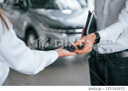 Keys of new automobile. Close up view. Man with woman in white clothes are in the car dealership together Keys of new automobile. Close up view. Man with woman in white clothes are in the car dealership together 125141633