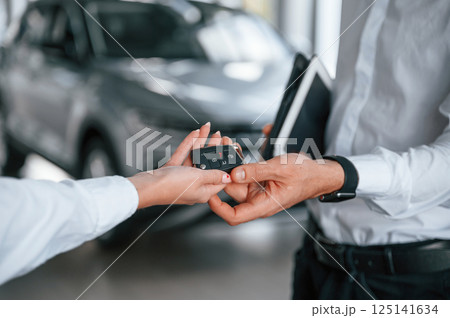 Keys of new automobile. Close up view. Man with woman in white clothes are in the car dealership together Keys of new automobile. Close up view. Man with woman in white clothes are in the car dealership together 125141634