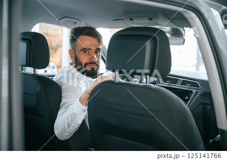 Looking behind. Young man in white clothes is in the car dealership Looking behind. Young man in white clothes is in the car dealership 125141766