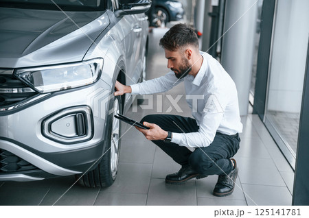 Checking the wheels. Young man in white clothes is in the car dealership Checking the wheels. Young man in white clothes is in the car dealership 125141781