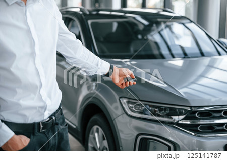 Closing the automobile by remote keys. Young man in white clothes is in the car dealership Closing the automobile by remote keys. Young man in white clothes is in the car dealership 125141787