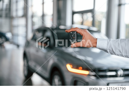 Closing the automobile by remote keys. Young man in white clothes is in the car dealership 125141790