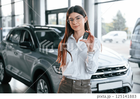Holding keys. Young woman in white formal clothes is in the at dealership Holding keys. Young woman in white formal clothes is in the at dealership 125141883