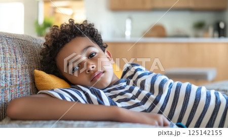 Relaxed young boy lounging on couch at home in striped shirt. Little biracial patient 125142155
