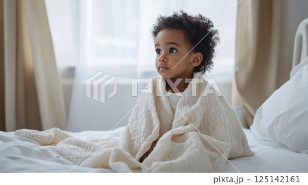 Cozy morning moments with adorable child wrapped in soft blanket. Little biracial patient 125142161