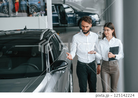 Walking and looking at the automobile. Man with woman in white clothes are in the car dealership together Walking and looking at the automobile. Man with woman in white clothes are in the car dealership together 125142224