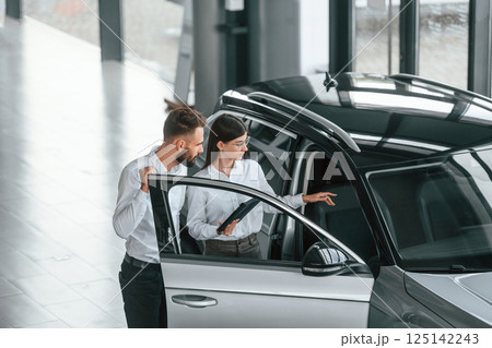 Door is opened. Man with woman in white clothes are in the car dealership together Door is opened. Man with woman in white clothes are in the car dealership together 125142243