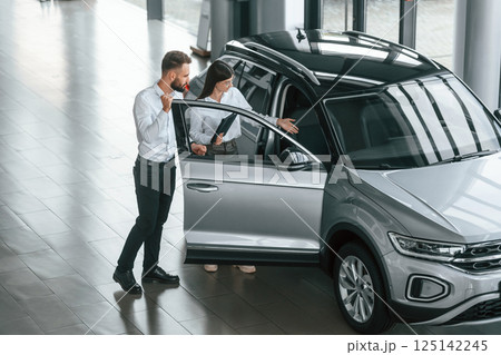Door is opened. Man with woman in white clothes are in the car dealership together Door is opened. Man with woman in white clothes are in the car dealership together 125142245