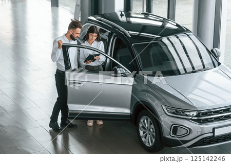 Door is opened. Man with woman in white clothes are in the car dealership together 125142246