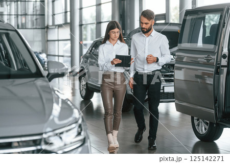 Front view. Man with woman in white clothes are in the car dealership together 125142271