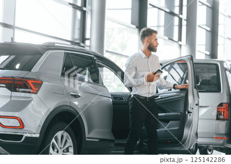 Walking out of automobile. Young man in white clothes is in the car dealership 125142286