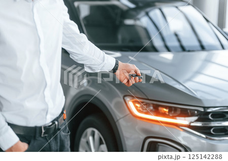 Using the keys remote controller. Young man in white clothes is in the car dealership Using the keys remote controller. Young man in white clothes is in the car dealership 125142288