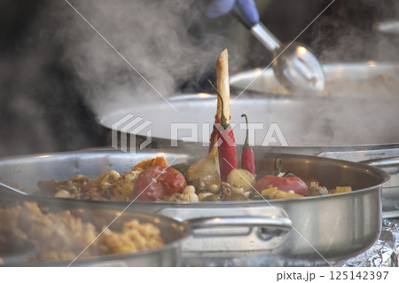 Steaming plov simmers in large metal pots, a flavorful Central Asian rice dish with vegetables. 125142397