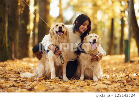 Sitting on the ground and embracing the animals. Woman on the walk with her two dogs in the autumn forest Sitting on the ground and embracing the animals. Woman on the walk with her two dogs in the autumn forest 125142524