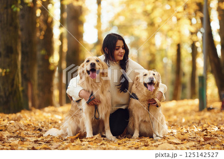 Sitting on the ground and embracing the animals. Woman on the walk with her two dogs in the autumn forest Sitting on the ground and embracing the animals. Woman on the walk with her two dogs in the autumn forest 125142527