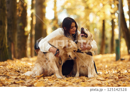 Sitting on the ground and embracing the animals. Woman on the walk with her two dogs in the autumn forest Sitting on the ground and embracing the animals. Woman on the walk with her two dogs in the autumn forest 125142528