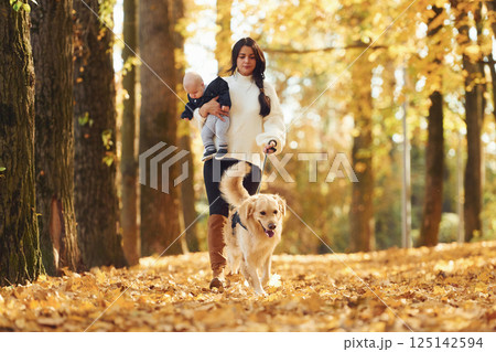 Mother with toddler and dog is having a walk in the autumn park 125142594