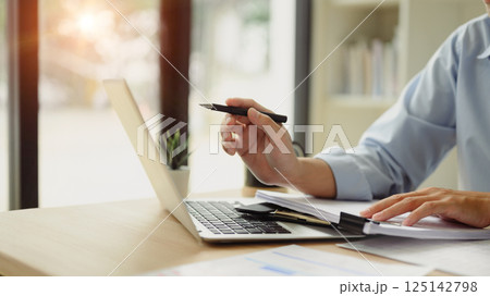 Businessman reviewing reports and working with laptop at desk Businessman reviewing reports and working with laptop at desk 125142798