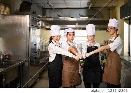 Group of students in uniform doing a group fist bump before starting their cooking session 125142801
