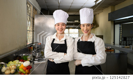 Confident culinary students in chef uniforms standing proudly in professional kitchen 125142827